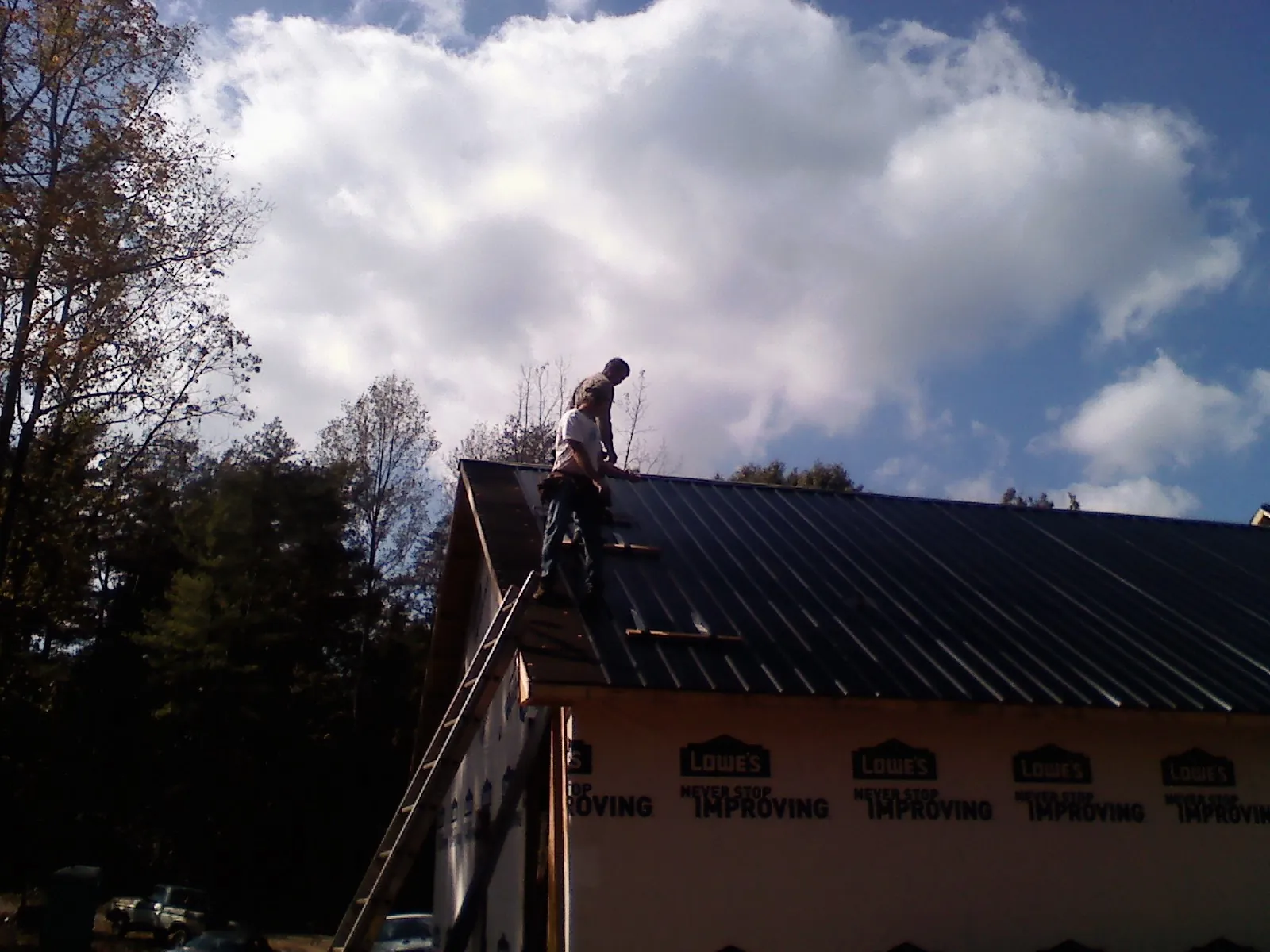 Roofer fastening dark metal panels high against a cloudy sky, from a Roof Inspection job in Weston
